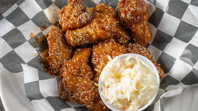 Sesame glazed chicken wings in a basket with a side of coleslaw